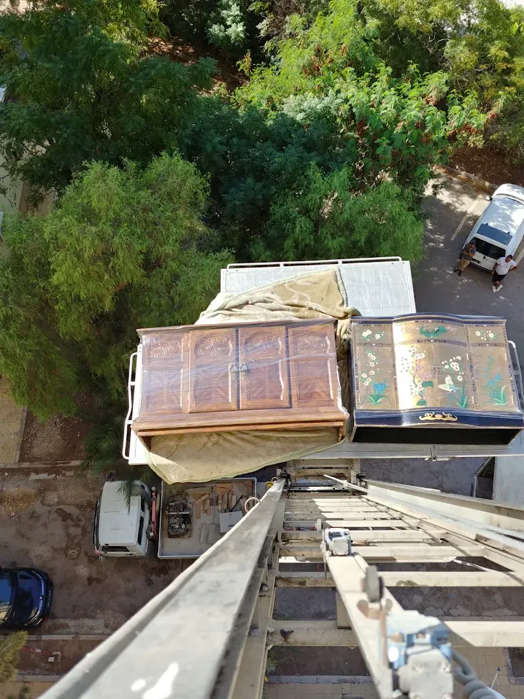 Monte-meuble Ben Aissa Transport descendant une armoire et un buffet emballés vers le camion de déménagement